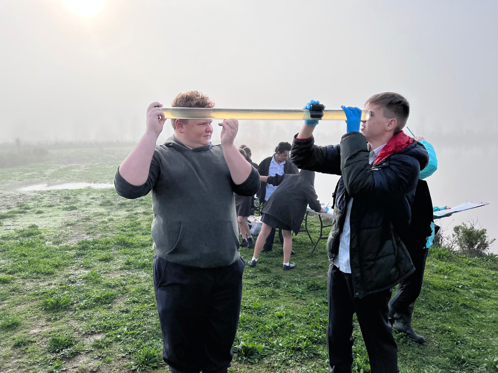 Two students reading a water clarity tube at the lake edge